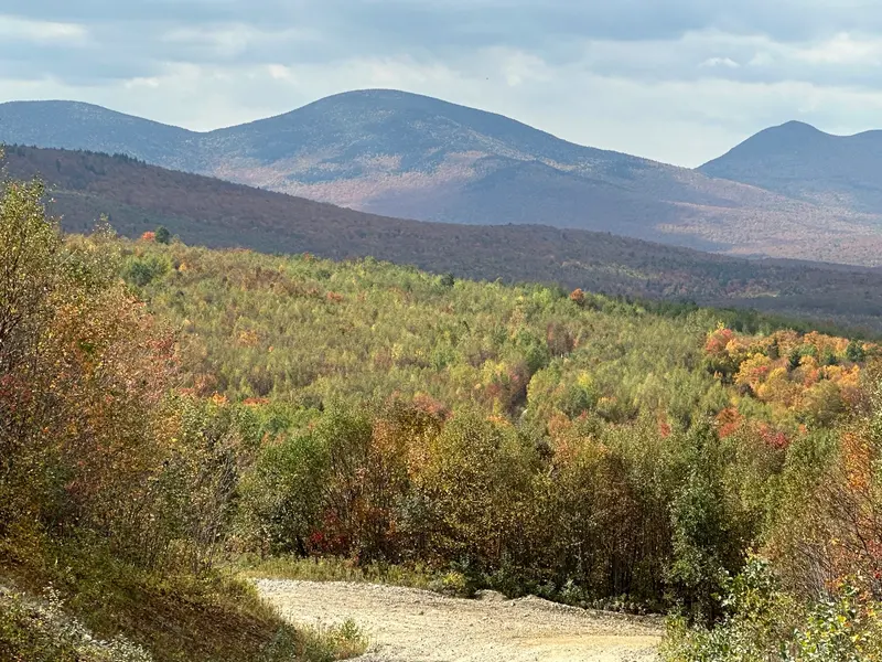 Gravel ATV trail winding through colorful fall forest toward New Hampshire mountains